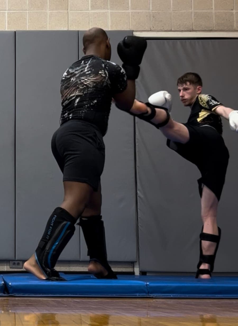 Will H. training high kicks with a partner on the mats